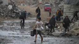 Diketahui, sekitar 85% infrastruktur air dan sanitasi di Gaza telah rusak atau hancur akibat serangan militer Israel dalam dua tahun terakhir. Tampak dalam foto, seorang anak laki-laki membawa dua ember kosong saat berjalan menuju tempat mengambil air di tengah hujan deras di kawasan Sheikh Radwan, Kota Gaza, Jumat 14 November 2025. (AP Photo/Jehad Alshrafi)