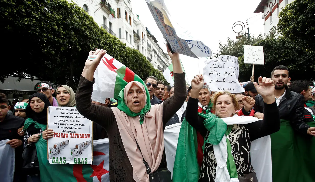 Demonstran memegang bendera dan spanduk saat berunjuk rasa di Aljir, Aljazair, Jumat (19/4). Demonstrasi sudah memasuki pekan ke kesembilan. (REUTERS/Ramzi Boudina)