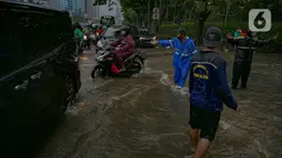 Petugas mengatur kelancaran lalu lintas saat air menggenangi ruas Jalan Gatot Subroto, Jakarta, Kamis (18/2/2021). Hujan deras yang mengguyur wilayah Jakarta menyebabkan terjadinya genangan di beberapa ruas jalan, meski begitu sejauh ini kendaraan masih dapat melintas. (Liputan6.com/Faizal Fanani)