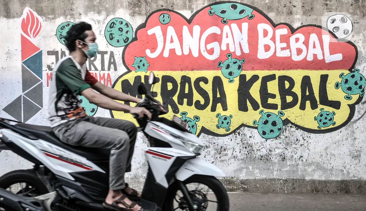 Pengendara motor melintasi mural bertema imbauan protokol kesehatan COVID-19 di kawasan Cakung Barat, Jakarta, Minggu (18/10/2020). Mural karya warga setempat tersebut bertujuan mengingatkan masyarakat akan pentingnya memakai masker, menjaga jarak, dan mencuci tangan. (merdeka.com/Iqbal S. Nugroho)