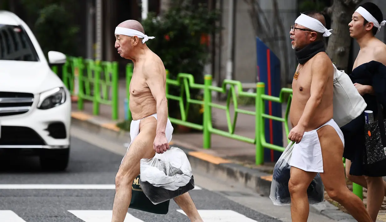 Orang-orang percaya Shinto dari Kuil Teppozu Inari tiba untuk mandi di air dingin untuk memurnikan jiwa dan tubuh mereka selama ritual Tahun Baru di Tokyo (12/1/2020). Sekitar 100 orang percaya Shinto ambil bagian dalam ritual tahunan tersebut. (AFP/Charly Triballeau)