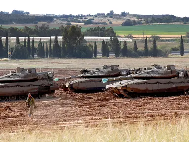 Seorang tentara Israel berjalan melewati tank Merkava yang terparkir di dekat perbatasan dengan Jalur Gaza, Israel, Senin (6/5/2019). Para pemimpin Palestina di Gaza menyetujui gencatan senjata dengan Israel. (JACK GUEZ/AFP)