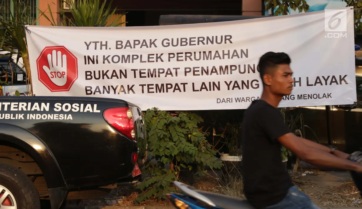 Pengendara motor melintasi spanduk penolakan lokasi penampungan pencari suaka di Kalideres, Jakarta, Selasa (16/7/2019). Sejak Kamis (11/7) para pencari suaka dipindahkan dari di pinggir jalan dan trotoar di kawasan Kebon Sirih ke bekas Markas Kodim di Kalideres . (Liputan6.com/Helmi Fithriansyah)