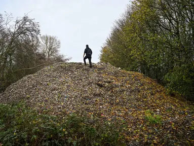 Aktivis lingkungan merekam konten untuk media sosial di tumpukan besar sampah yang dibuang sembarangan, yang ditumpuk di sebuah ladang antara Sungai Cherwell dan Jalan A34 dekat Kidlington, Oxfordshire, di barat London pada 16 November 2025. Gunungan atau tumpukan sampah ilegal berukuran raksasa ditemukan di sebuah ladang di tepi Sungai Cherwell dekat Kidlington, Oxfordshire, Inggris. (Justin TALLIS/AFP)