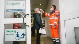 Seorang petugas medis mengukur suhu tubuh pengunjung di pintu masuk pusat vaksinasi COVID-19 di pusat pameran Essen di Essen, Jerman (12/12/2020). (Xinhua/Tang Ying)
