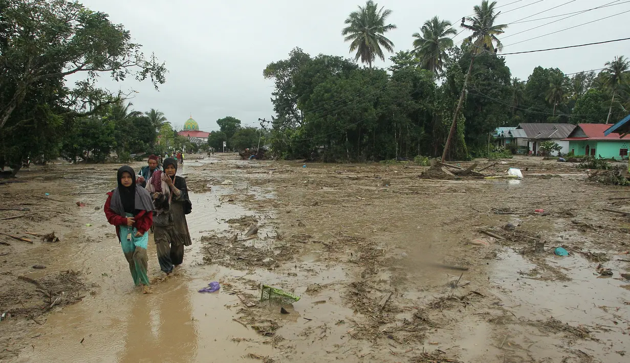 Penduduk desa berjalan melalui daerah banjir di desa Radda di Kabupaten Luwu Utara, Sulawesi Selatan (14/7/2020). Akibat musibah banjir bandang ini setidaknya sekitar 15 orang tewas dan belasan lainnya dinyatakan hilang. (AFP/Aryanto)
