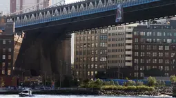 Sebuah kapal melintas di bawah banner bergambar Presiden Rusia Vladimir Putin yang tergantung di Jembatan Manhattan, New York, Kamis (6/10). Terdapat tulisan ‘PEACEMAKER’ (pendamai) yang dicetak tebal pada banner tersebut. (REUTERS/Brendan McDermid)