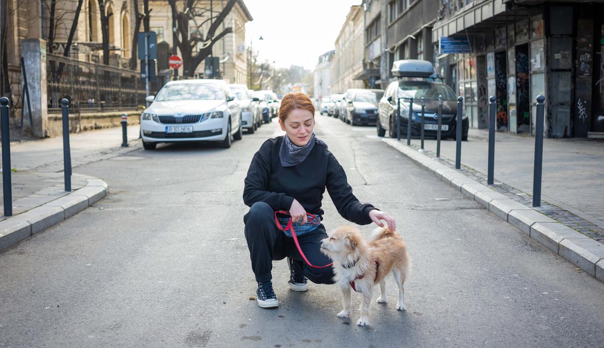 Andra Aron (32) berpose dengan anjingnya Gerald (4) saat perjalanan di Bucharest (28/3/2020). Undang-undang militer, yang disahkan pemerintah Rumania untuk mengurangi penyebaran virus corona, menyatakan berjalan bersama anjing adalah salah satu  kegiatan yang masih diizinkan. (AFP/Andrei Pungovschi)