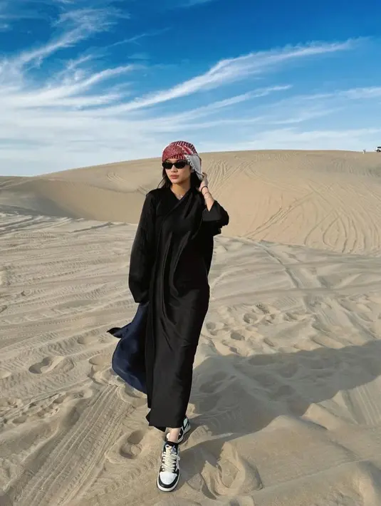 Azizah mengenakan dress hitam dipadukan outer warna serasi saat berkunjung ke gurun pasir. Ia juga mengenakan sorban di atas kepalanya. [@azizahsalsha_]