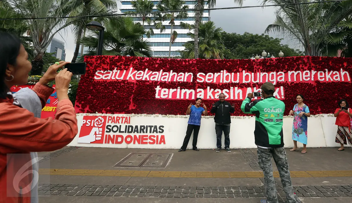 Warga berfoto di depan karangan bunga untuk Basuki T Purnama dan Djarot Sjaiful Hidayat di Balai Kota Jakarta, Selasa (25/4). Karangan bunga tersebut terus bertambah berisi simpati warga kepada Ahok-Djarot pascapilkada DKI 2017. (Liputan6/Johan Tallo)