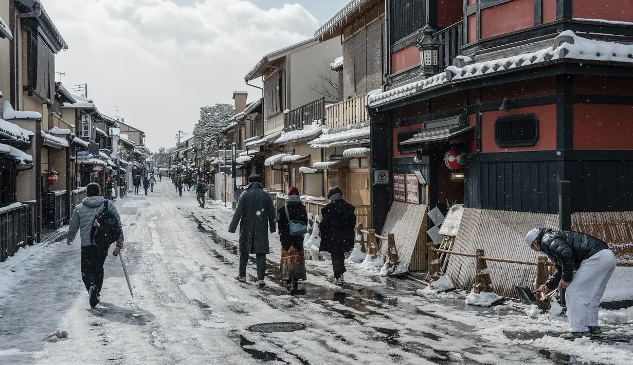 Orang-orang melintasi Jalan Hanamikoji setelah salju tebal dan angin kencang semalaman mempengaruhi wilayah luas negara itu di Kyoto, Jepang, Rabu (25/1/2023). Karena pola musim dingin yang keras diperkirakan akan berlangsung hingga Kamis (26/1), beberapa daerah di Jepang dapat mengalami suhu terendah dalam satu dekade. (Fred Mery / AFP)