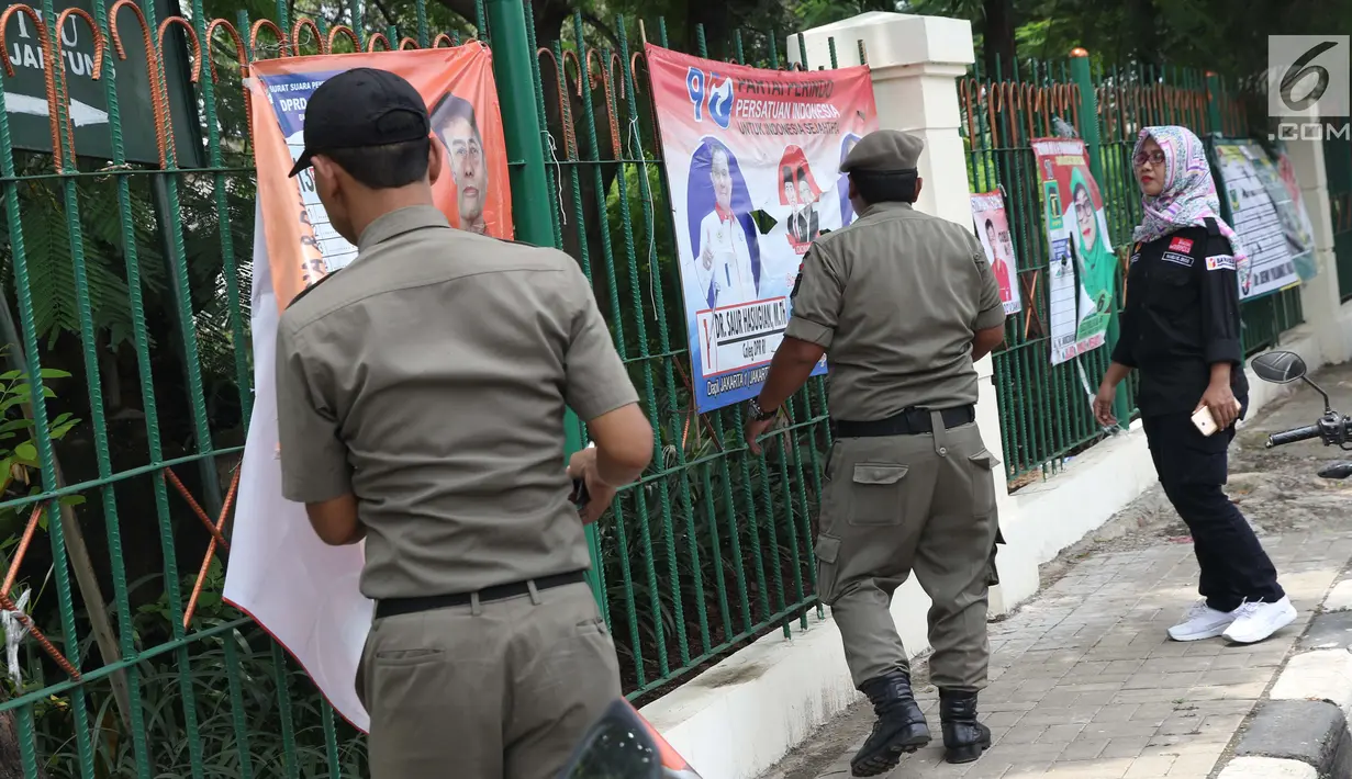 Petugas Satpol PP bersama Panwaslu kecamatan Ciracas menurunkan APK yang terpasang di pagar pembatas antara jalan dengan taman di pinggir kali di sekitar Jalan Raya Bogor, Jakarta, Rabu (23/1). (Liputan6.com/Helmi Fithriansyah)