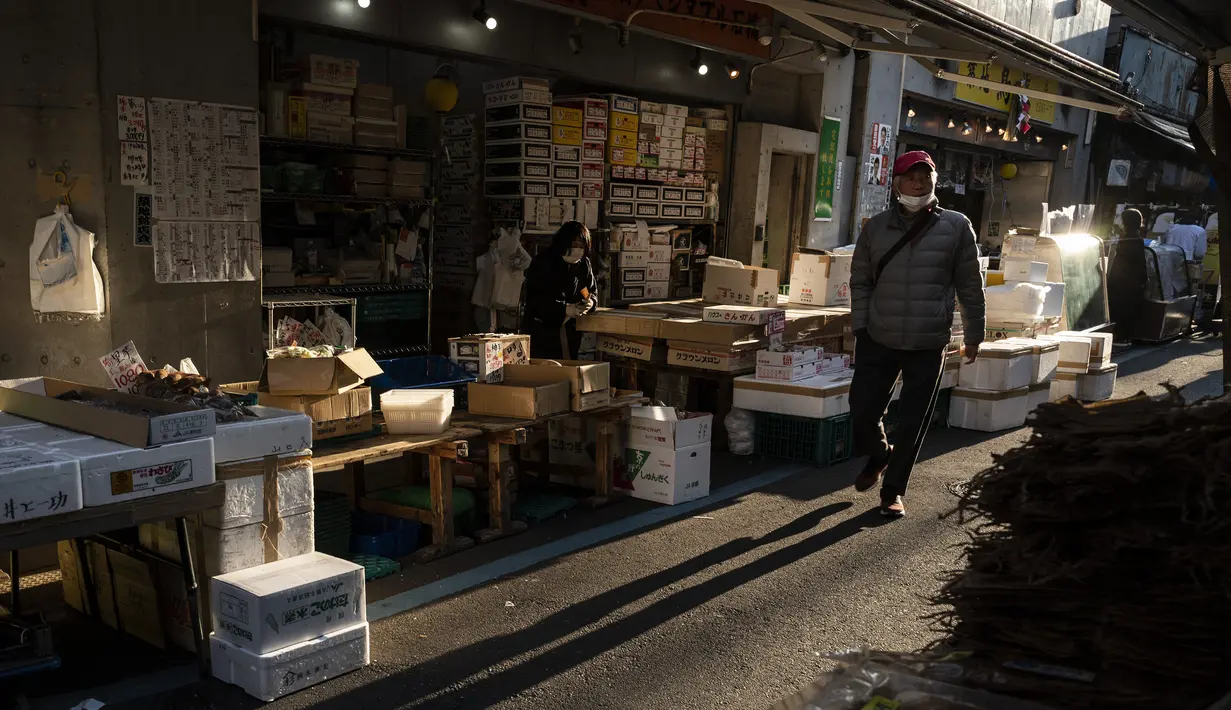 Seorang pria berjalan melalui jalan di daerah "pasar ikan luar" Tsukiji di Tokyo pada 28 Desember 2022. Menjelang liburan Tahun Bar, turis asing dan penduduk lokal berkunjung  ke pasar itu untuk menikmati hidangan bermacam makanan laut. (AFP/Richard A. Brooks)