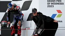 Pembalap Aprilia Racing, Maverick Vinales (kanan), memakai kostum Batman saat menaiki podium juara MotoGP Mandalika 2023 setelah menjalani balapan di Mandalika International Street Circuit, Lombok, Minggu (15/10/2023) siang WIB. (AFP/Sonny Tumbelaka)