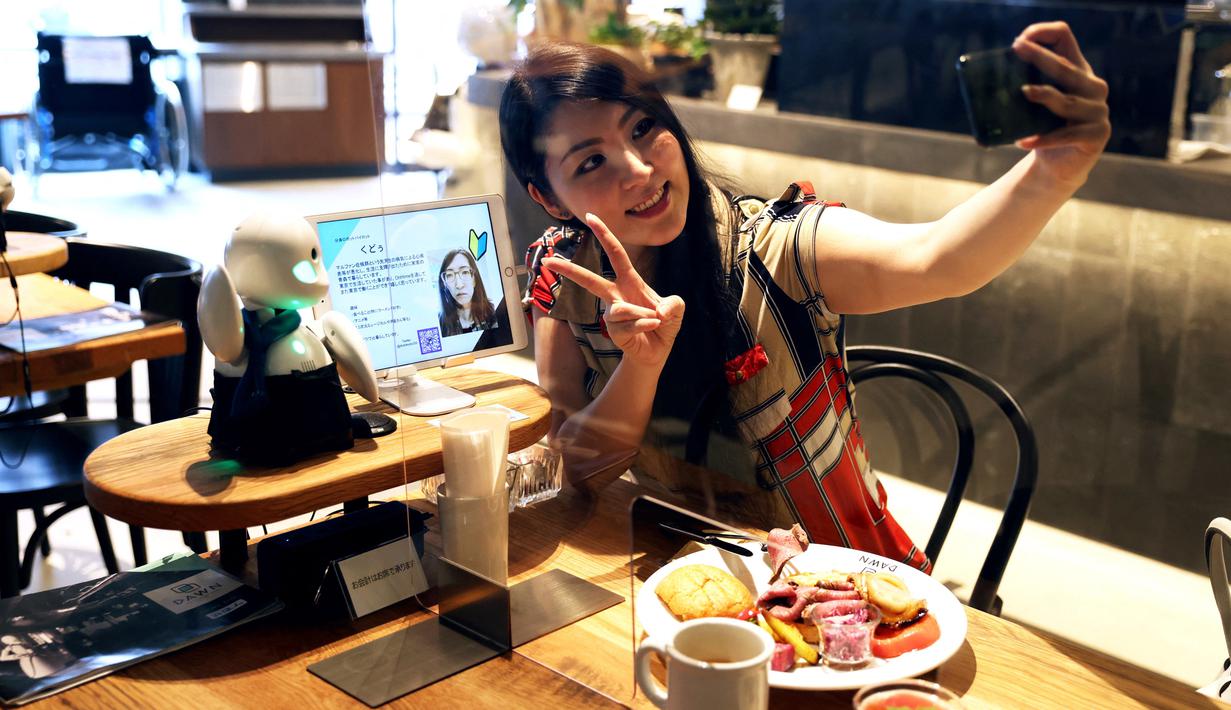 Seorang pelanggan berswafoto dengan robot humanoid mini bernama OriHime di Dawn Cafe, Tokyo, Jepang, 17 Agustus 2021. Peluncuran kafe ini bersamaan dengan Paralimpiade yang akan dibuka pada 24 Agustus. (Behrouz MEHRI/AFP)