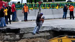 Petugas menggunakan derek turun ke dasar sebuah lubang yang tiba-tiba muncul di jalan raya Meksiko-Cuenava, Meksiko, Rabu (12/7). Lubang tersebut menelan seorang ayah dan putranya yang tengah berkendara dengan mobil. (AP/Tony Rivera)