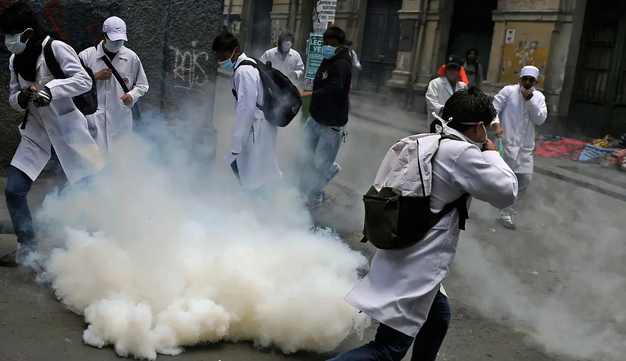 Mahasiswa kedokteran menghindar dari gas air mata saat demonstrasi dekat lapangan Murilo di La Paz, Bolivia (19/12). Para mahasiswa memprotes undang-undang baru Presiden Evo Morales terkait sanksi pidana malapraktik medis. (AFP Photo/Jorge Bernal)