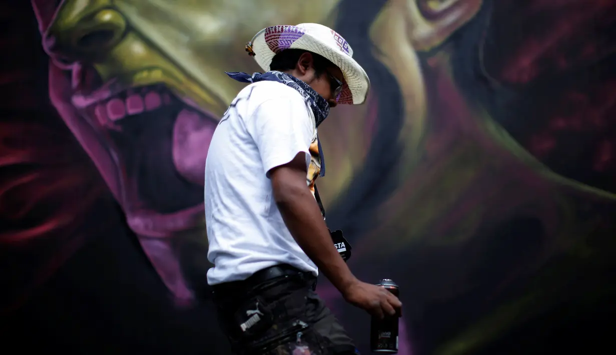 Seorang seniman yang bernama Montalvo Tekuene melewati salah satu karya grafiti dalam festival pekan grafiti di Mexico City, Meksiko, Minggu (9/10). Grafiti merupakan salah satu seni jalanan yang populer hingga kini. (REUTERS/Carlos JASSO)
