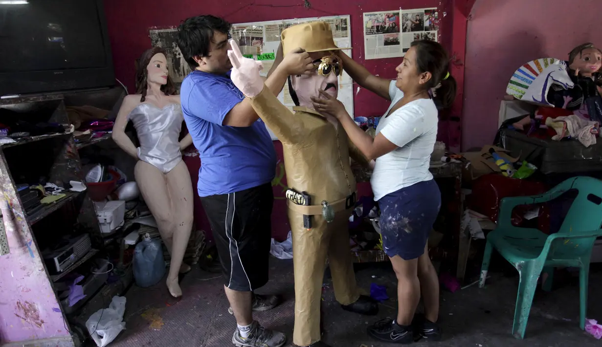 Dua orang pekerja memasangkan topi ke boneka raja narkoba Joaquin "El Chapo" Guzman saat menyelesaikannya di Reynosa, Meksiko (21/7/2015). Guzman melarikan diri dari penjara melalui terowongan yang ia buat pada bulan lalu. (REUTERS/Daniel Becerril)