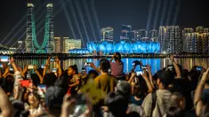 Orang-orang berkumpul di kawasan pejalan kaki Sungai Qiantang untuk menyaksikan pertunjukan cahaya di Hangzhou Olympic Sports Centre Stadium (kanan) menjelang Asian Games 2023 di Hangzhou, Provinsi Zhejiang, China, Selasa (19/9/2023). Hangzhou Olympic Sports Centre Stadium merupakan lokasi pembukaan Asian Games 2023. (Philip FONG/AFP)