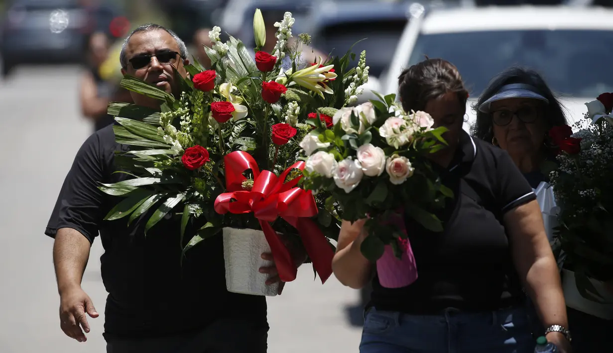 Orang-orang membawa bunga saat berjalan menuju tugu peringatan di luar Robb Elementary School untuk menghormati para korban yang tewas dalam penembakan di sekolah pekan ini, Uvalde, Texas, Amerika Serikat, 28 Mei 2022. (AP Photo/Dario Lopez-Mills)