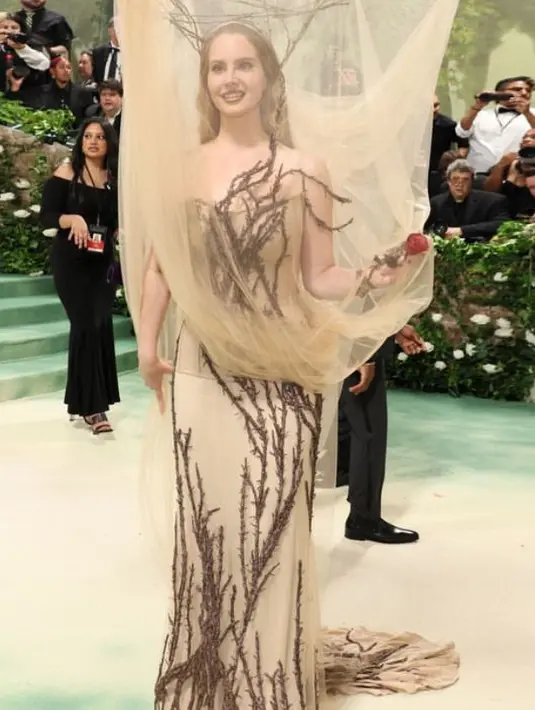 Lana Del Rey mengenakan gaun dari Alexander McQueen. Ia pun tampil sesuai dengan tema dengan siluet cabang-cabang pohon yang menyembul dari kanopi tulle. Dengan gaun tube coklat yang memiliki aksen motif akar. [@alexandermcqueen]
