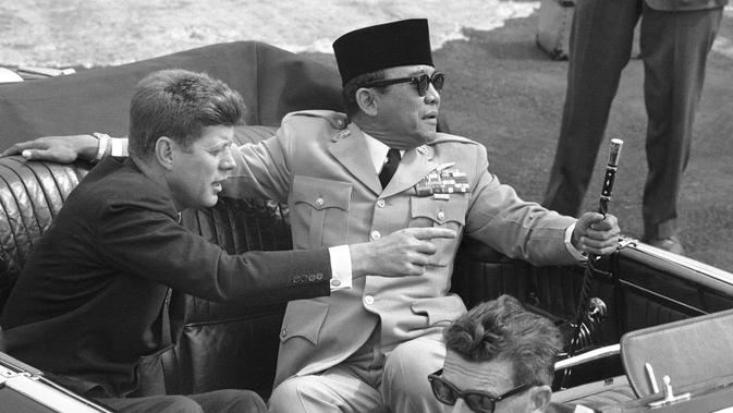 Presiden Amerika John Kennedy menunjuk Presiden Republik Indonesia Sukarno saat mereka duduk di mobil terbuka sesaat sebelum berangkat di Pangkalan Angkatan Udara Andrews, Washington, 24 April 1961. (AP Photo)