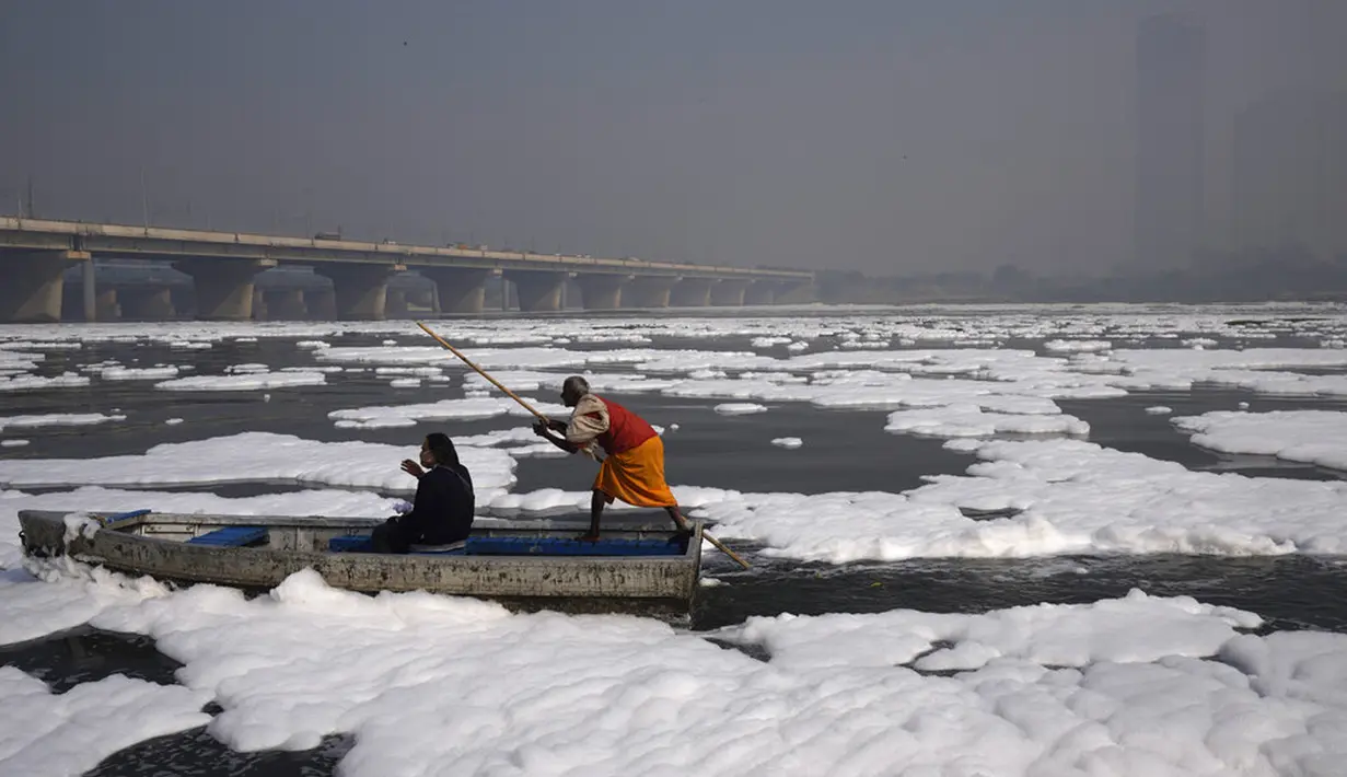 Seseorang naik perahu di Sungai Yamuna yang tertutup busa kimia karena polusi industri dan domestik saat cakrawala diselimuti kabut asap beracun, New Delhi, India, 17 November 2021. Indeks Kualitas Udara di New Delhi mencapai 499 dari 500. (AP Photo/Manish Swarup)
