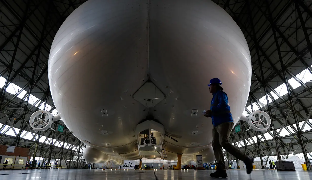 Petugas berjalan di depan The Airlander 10 saat peluncuran media di Cardington Airfield, Bedfordshire, Senin (21/3). Pesawat ini memiliki panjang  90 meter dan mempunyai lambung besar yang bisa dimasuki sebuah pesawat komersial. (ADRIAN DENNIS/AFP)