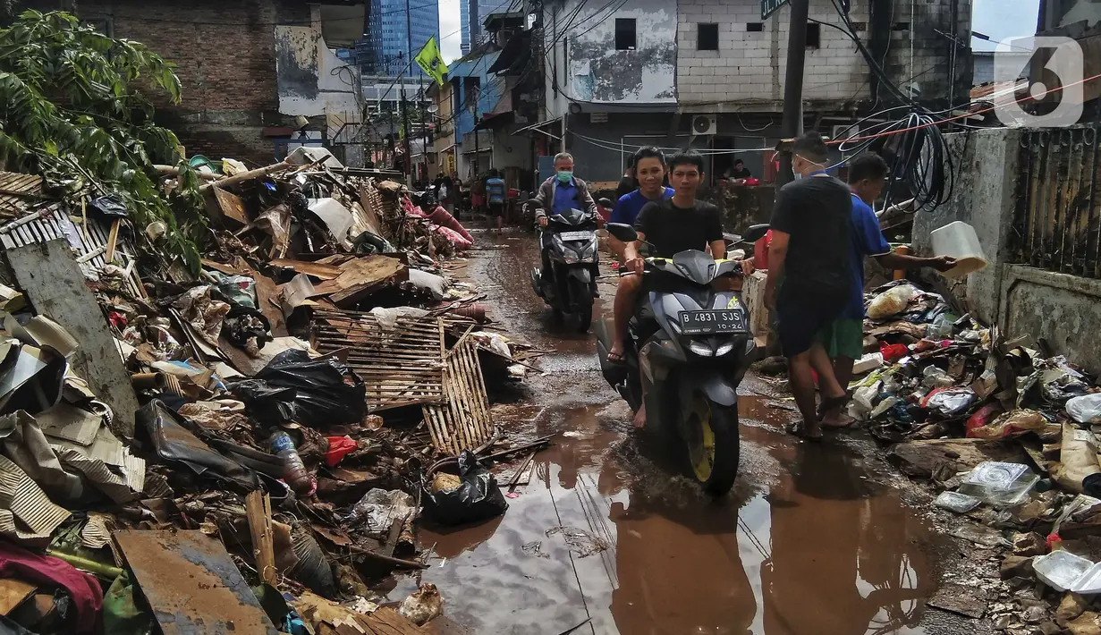 Pengendara sepeda motor melintas saat warga membersihkan sampah sisa banjir di Kebalen, Jakarta, Minggu (21/2/2021). Banjir yang terjadi kemarin karena curah hujan yang tinggi meninggalkan sampah di rumah warga. (Liputan6.com/Johan Tallo)