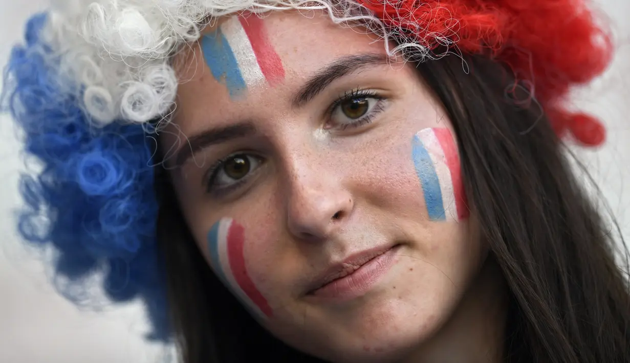 Suporter wanita melukis bendera Prancis di wajahnya sebelum menyaksikan pertandingan melawan Norwegia pada grup A Piala Dunia Wanita 2019 di Stadion Nice, Prancis (12/6/2019). Dalam pertandingan ini Prancis menang tipis atas Norwegia 2-1. (AFP Photo/Christophe Simon)