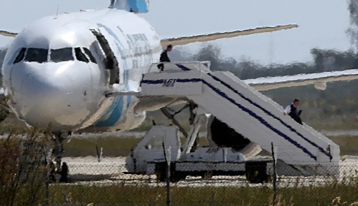 Seif Eldin Mustafa bersama seorang sandera saat akan turun dari pesawat EgyptAir, Siprus, Selasa (29/3). Aksi nekat Mustafa hingga membajak EgyptAir masih diselidiki petugas. (Reuters/Yiannis Kourtoglou)
