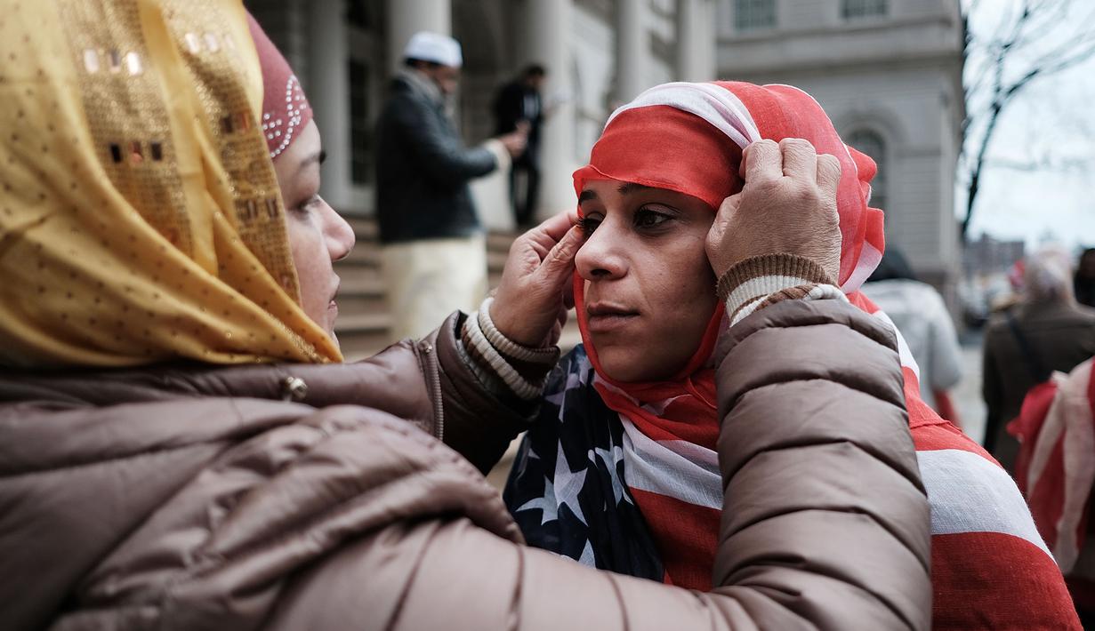 Seorang wanita membantu rekannya memakai kerudung bermotif bendera AS saat perayaan Hari Hijab Sedunia di depan Balai Kota, New York, Rabu (1/2). Hari Hijab Sedunia digagas oleh warga New York bernama Nazma Khan. (Spencer Platt / Getty Images / AFP)