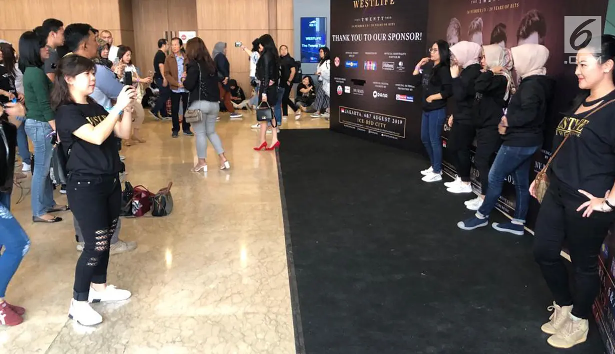 Penonton berfoto dengan latar belakang banner konser "Westlife-The Twenty Tour 2019" di ICE BSD, Tangerang, Banten, Selasa (6/8/2019). Shane Filan, Nicky Byrne, Mark Feehily, dan Kian Egan siap memberikan yang terbaik untuk para penggemarnya di Indonesia. (Liputan6.com/Fery Pradolo)