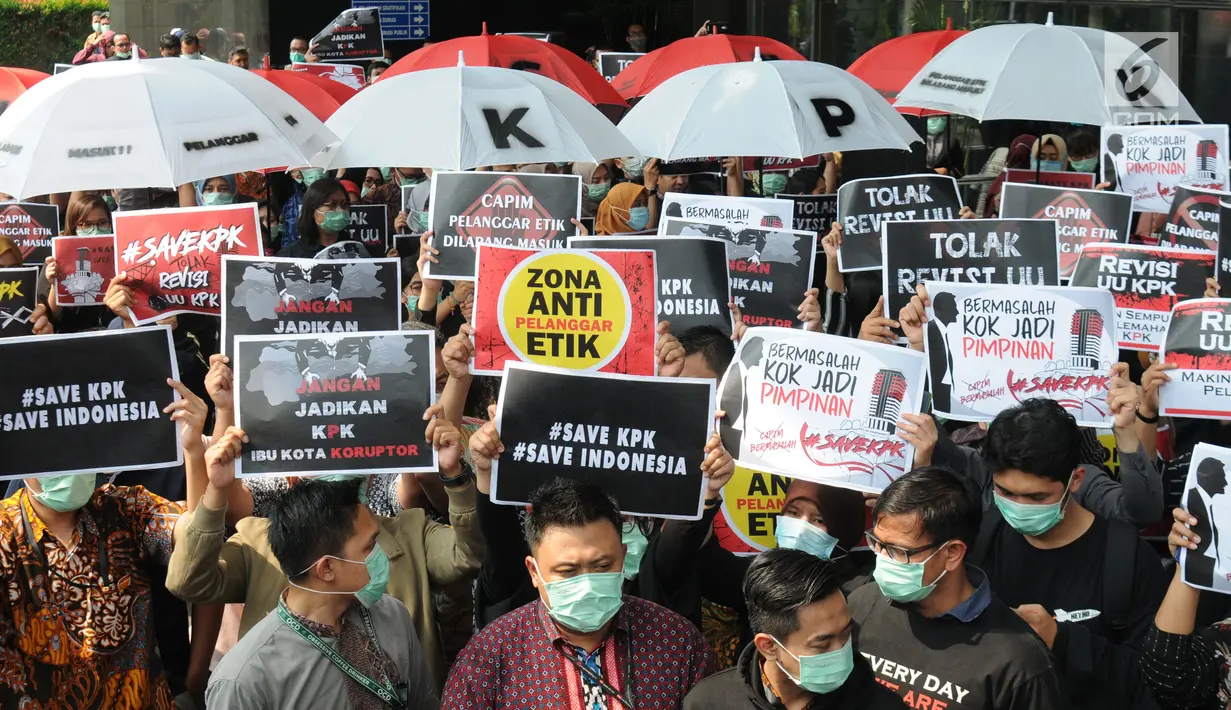 Pegawai KPK membawa poster saat menggelar aksi di Lobi Gedung KPK, Kuningan, Jakarta, Jumat (6/9/2019). Dalam aksi menolak revisi UU KPK tersebut, mereka mengenakan baju serba hitam lengkap dengan masker penutup mulut dan membawa payung. (merdeka.com/Dwi Narwoko)