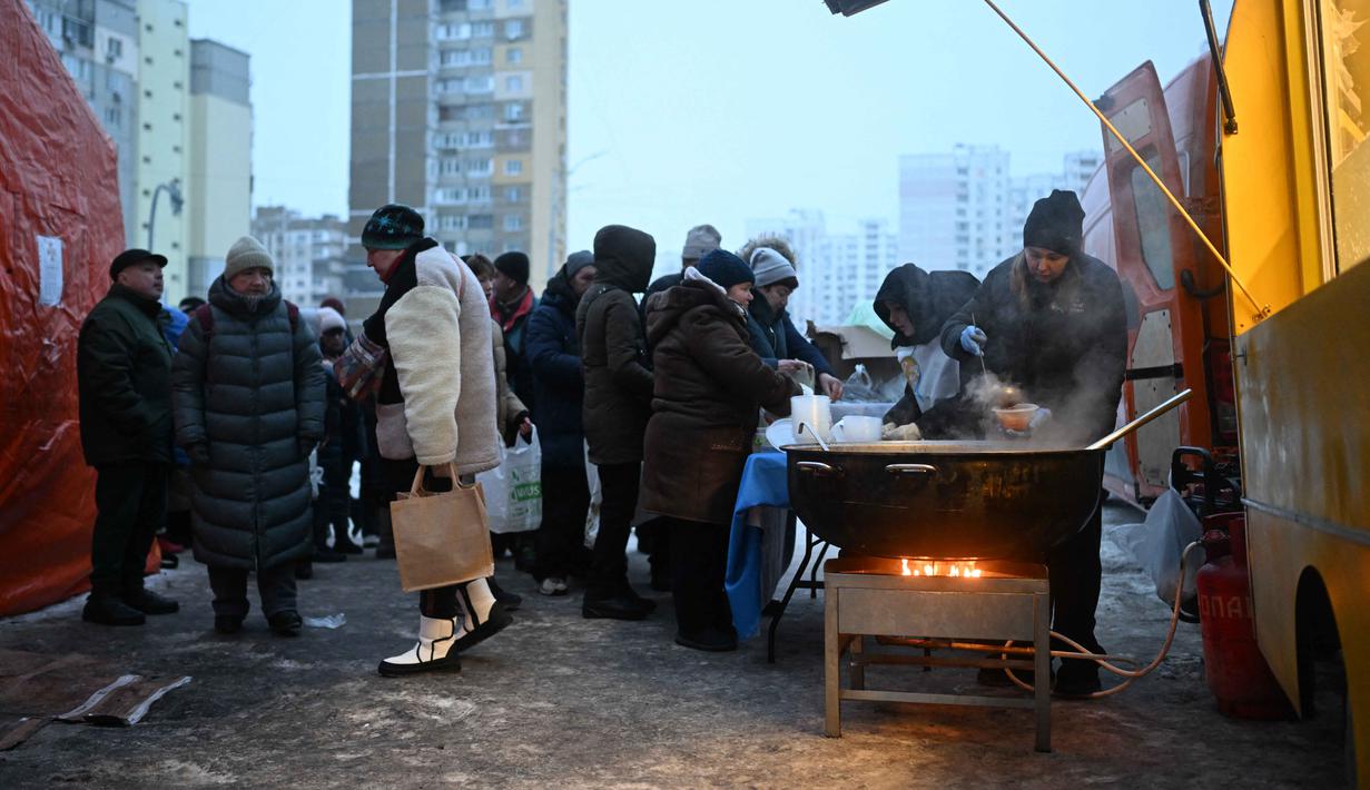 Terdampak pemadaman listrik dan air, warga Kyiv terlihat mengantre untuk mendapatkan makanan hangat di tengah kondisi musim dingin yang ekstrem. Tampak dalam foto, para sukarelawan dari organisasi amal makanan yang berbasis di Amerika Serikat (AS), World Central Kitchen, membagikan makanan hangat kepada warga setempat di sebuah kawasan perumahan di Kyiv yang mengalami pemadaman listrik dan air akibat serangan Rusia yang menghantam sektor energi, Kamis 22 Januari 2026. (Sergei GAPON/AFP)