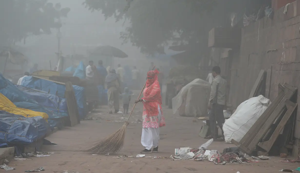 Petugas kebersihan menyapu jalan di ibu kota India, New Delhi yang diselimuti kabut asap, Rabu (8/11). Indian Medical Association menyarankan warga untuk tidak keluar rumah dan menghindari sedapat mungkin aktivitas fisik apapun. (SAJJAD HUSSAIN/AFP)