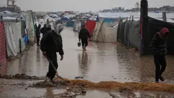 Puluhan hingga ratusan tenda pengungsi Palestina di wilayah tersebut terendam banjir. Tampak dalam foto, warga Palestina berjalan melewati kamp tenda yang terendam banjir setelah hujan lebat di Deir al-Balah, Jalur Gaza, Kamis 11 Desember 2025. (AP Photo/Abdel Kareem Hana)