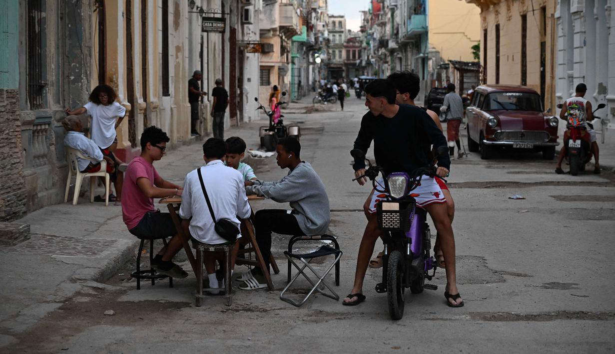 Ini merupakan kejadian kedua dalam sepekan terakhir dan yang ketiga sepanjang Maret 2026. Tampak dalam foto, warga Kuba bermain domino di jalanan tanpa listrik selama pemadaman listrik nasional di Havana, Kuba pada Sabtu 21 Maret 2026. (Yamil LAGE/AFP)