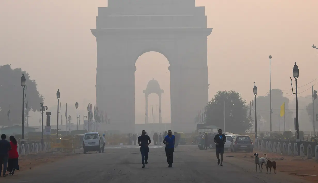 Sejumlah warga beraktivitas di dekat monumen India Gate di tengah kondisi kabut asap tebal di New Delhi (30/10). (AFP Photo/Dominique Faget)