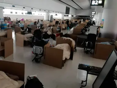 Orang-orang menunggu hasil tes virus corona mereka di tempat tidur sementara dari kotak kardus di Bandara Internasional Narita di Narita, dekat Tokyo, 8 April 2020. Bandara tersebut kini dipenuhi dengan bilik-bilik kardus yang berada di area pengambilan bagasi. (Naohiro Katsuta via AP)