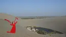 Seorang wanita berfoto bersama Air Mancur Bulan Sabit (kanan) di kawasan wisata Gunung Mingsha dan Air Mancur Bulan Sabit di Dunhuang, Jiuquan, Provinsi Gansu, Tiongkok Barat Laut, pada 19 Oktober 2025. (Adek BERRY/AFP)