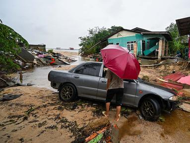 Seorang pria berjalan melewati sebuah mobil yang terdampar dan rumah-rumah yang rusak akibat banjir di Tumpat, negara bagian Kelantan, Malaysia, pada Rabu 4 Desember 2024. (MOHD RASFAN/AFP)