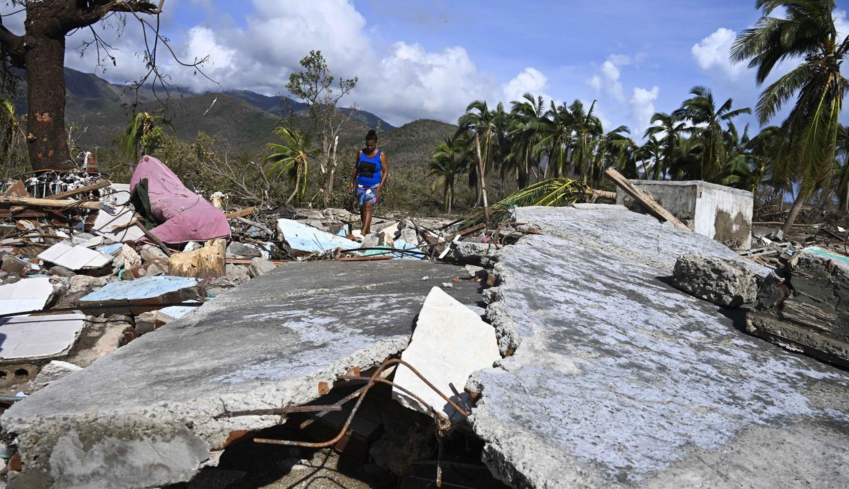 Seorang perempuan berjalan di tengah puing-puing rumah yang rusak akibat Badai Melissa di desa Boca de Dos Rios, provinsi Santiago de Cuba, Kuba pada Kamis 30 Oktober 2025. Badai Melissa menerjang Kuba dengan kecepatan angin maksimum sekitar 195 km/jam (120 mph). (YAMIL LAGE/AFP)