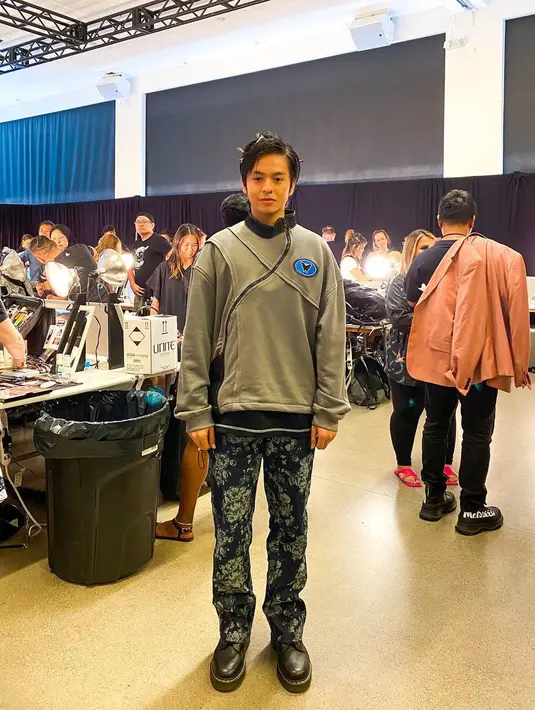 Angga Yunanda tampil di New York Fashion Week tahun ini membawakan koleksi busana rilisan Erigo-X. Salah satu foto memperlihatkan sang aktor mengenakan atasan lengan panjang abu-abu dengan aksen garis miring dan garis lenggok serupa benang layang-layang yang dipadukan dengan celana panjang berwarna dasar biru tua. Motifnya, serupa tumpukan kelopak bunga. (Foto: Dok. Instagram @anggayunandareal16)