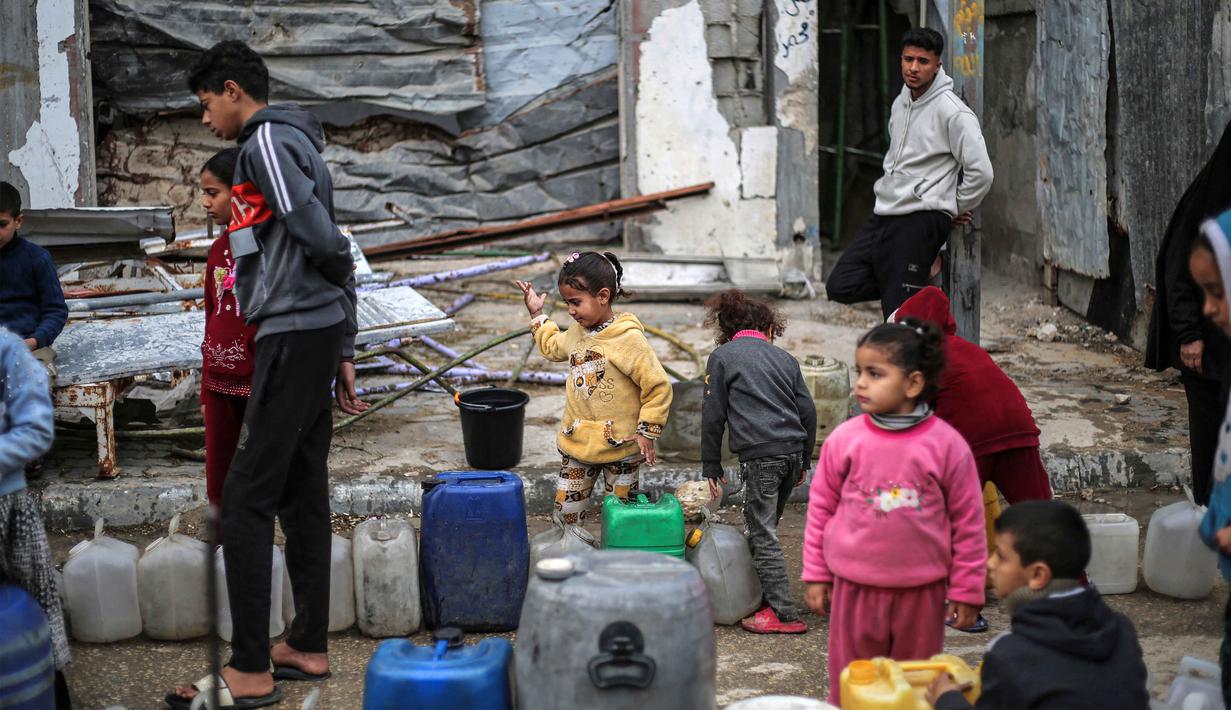 Risiko ini dampak fisik dan psikologis serta penghancuran sekolah yang disebabkan perang selama lebih dari dua tahun. Tampak dalam foto, orang-orang, termasuk anak-anak mengantre untuk mengisi wadah dengan air dari tangki portabel, di kamp pengungsi Palestina Nuseirat di utara Deir al-Balah, Jalur Gaza tengah pada 29 Januari 2026. (EYAD BABA/AFP)