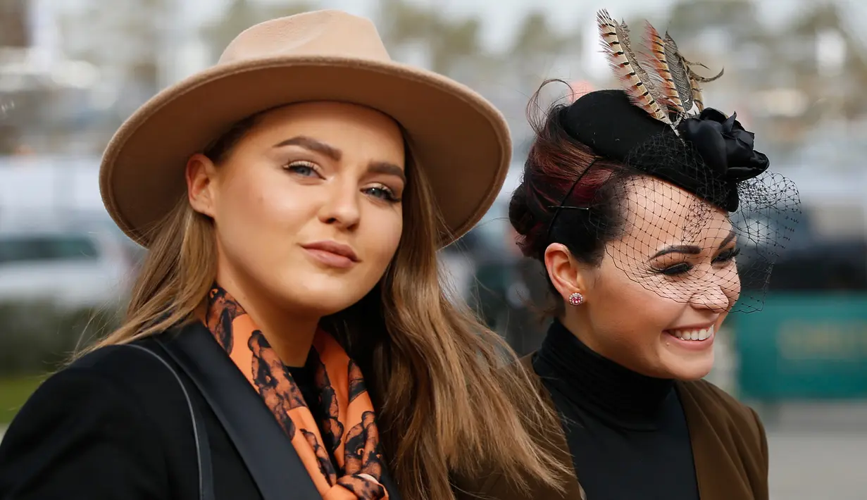 Dua pengunjung wanita, tampil cantik dengan topi di kepalanya jelang pembukaan ajang Pacuan Kuda dalam Festival Cheltenham di Inggris (16/3). Pacuan kuda merupakan olahraga yang disukai oleh kerajaan Inggris. (REUTERS/Paul Childs)
