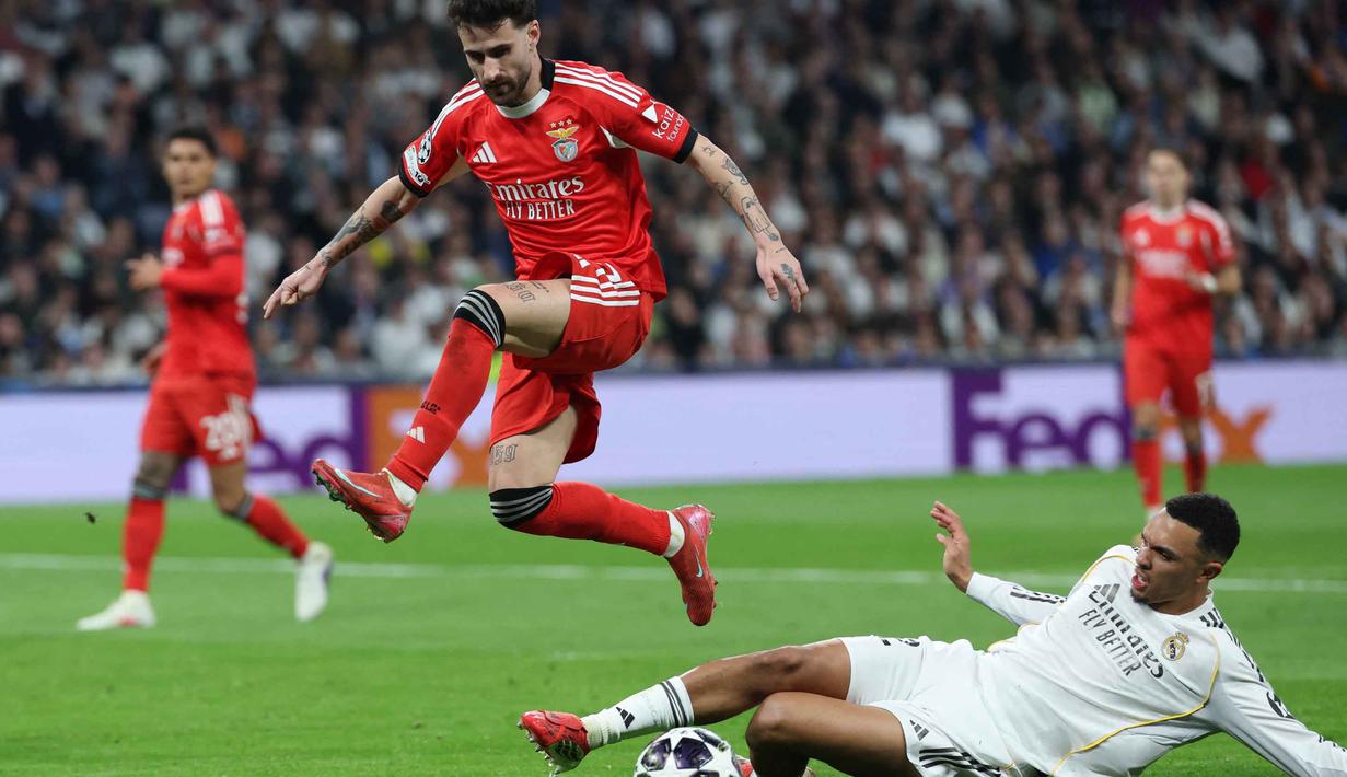 Hasil imbang 1-1 bertahan hingga waktu turun minum. Tampak dalam foto, gelandang SL Benfica, Rafa Silva, melompati bek Real Madrid asal Inggris, Trent Alexander-Arnold, selama pertandingan leg kedua babak playoff 16 besar Liga Champions 2025/2026 di Stadion Santiago Bernabeu pada Rabu 25 Februari 2026 waktu setempat atau Kamis (26/2/2026) dini hari WIB. (Thomas COEX/AFP)