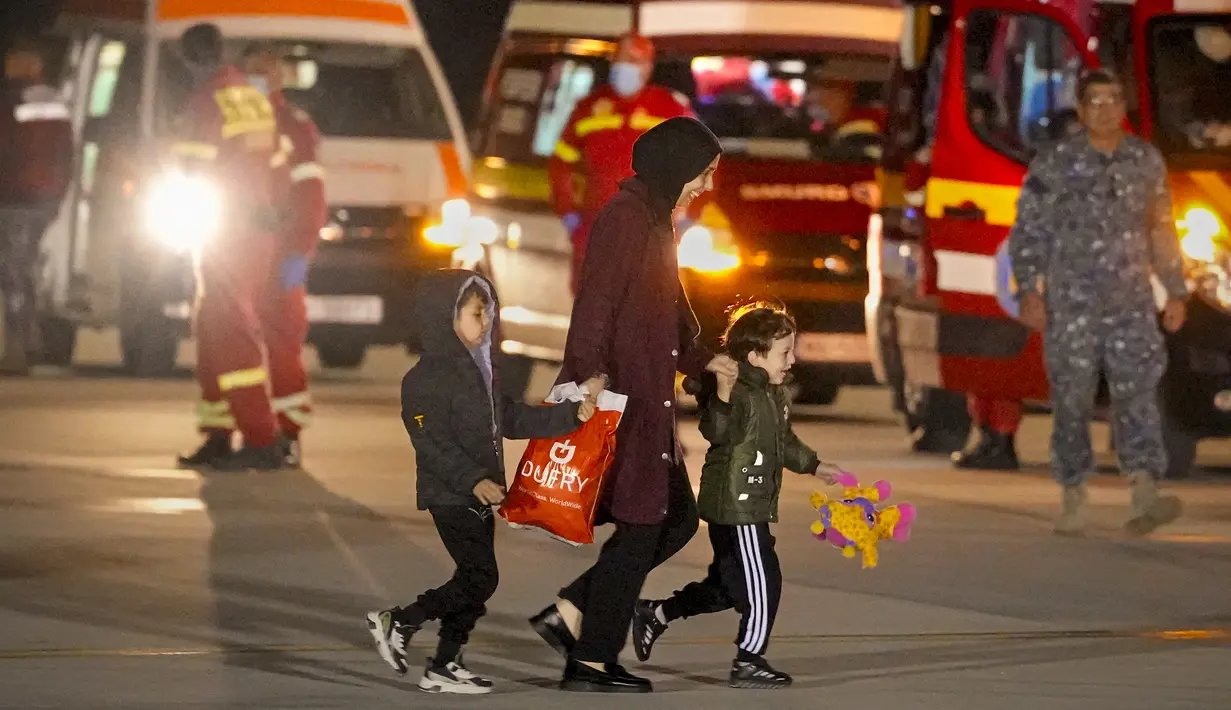 Seorang perempuan dan dua anak, dievakuasi dari Gaza, tersenyum saat berjalan di landasan setelah tiba dari Mesir di pangkalan angkatan udara Baza 90 di Otopeni, Rumania, Rabu, 8 November 2023. (AP Photo/Andreea Alexandru)