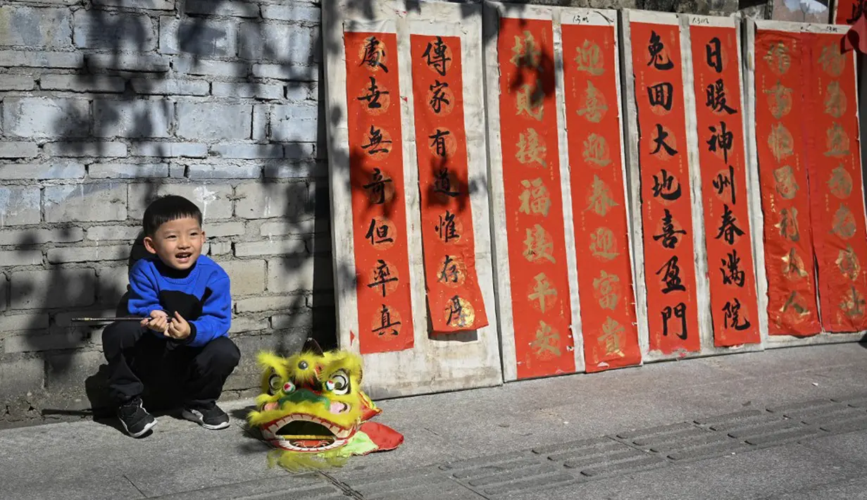 Seorang anak berpose untuk difoto di samping kuplet musim semi, semacam dekorasi Tahun Baru Imlek, jelang dimulainya Tahun Baru Imlek di sebuah kios di Foshan, Provinsi Guangdong, China, 18 Januari. Ada banyak versi dan gaya yang berbeda, tetapi setiap bait dalam kuplet menyampaikan keinginan penulis untuk tahun baru. (Giok Gao/AFP)